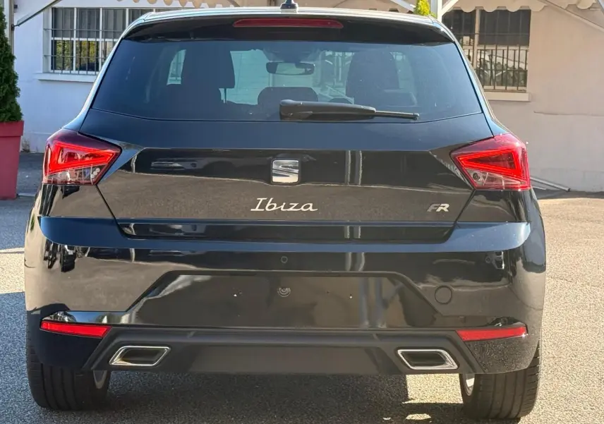 Vue arrière d'une SEAT Ibiza 1.0 TSI FR noire, avec feux LED triangulaires et double sortie d'échappement chromée.