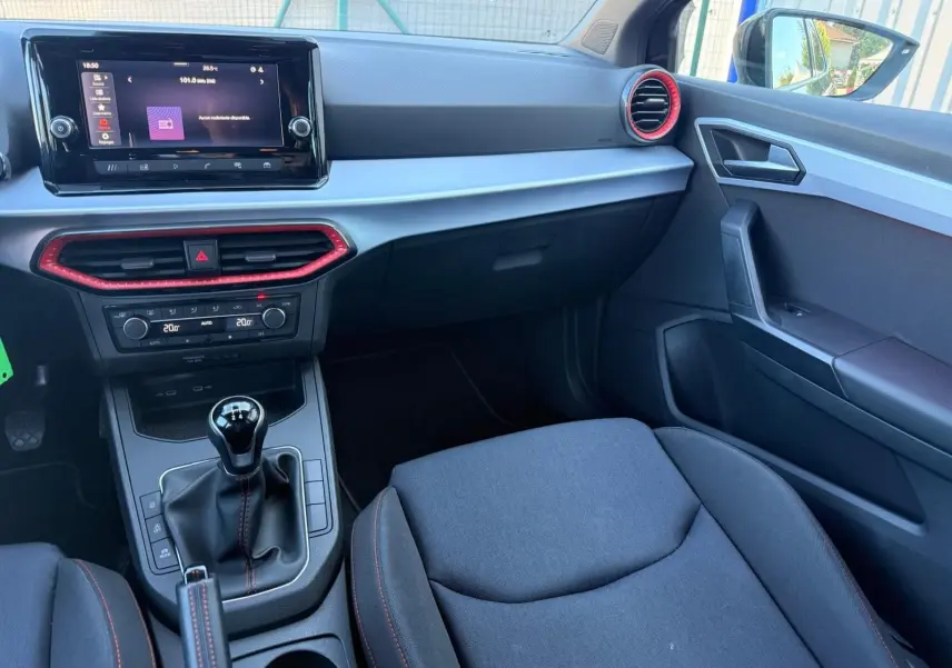 Intérieur avant droit de la SEAT Ibiza noire, tableau de bord avec écran tactile et détails rouges autour des aérateurs.
