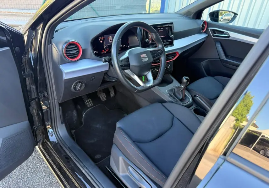 Intérieur côté conducteur d’une SEAT Ibiza noire 2025, volant cuir, détails rouges autour des aérateurs et écran tactile central.