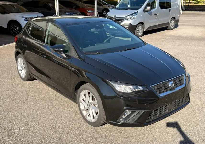 Vue 3/4 avant droite d'une SEAT Ibiza noire 2025 avec phares LED et jantes alliage argentées sur parking.