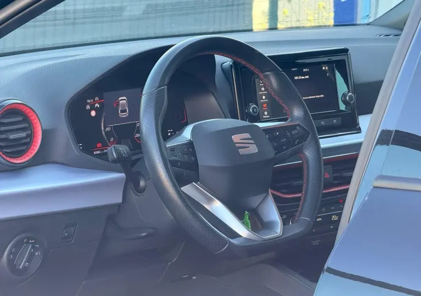 Vue intérieure du poste de conduite d'une SEAT Ibiza noire, volant cuir avec surpiqûres rouges et écran tactile central.