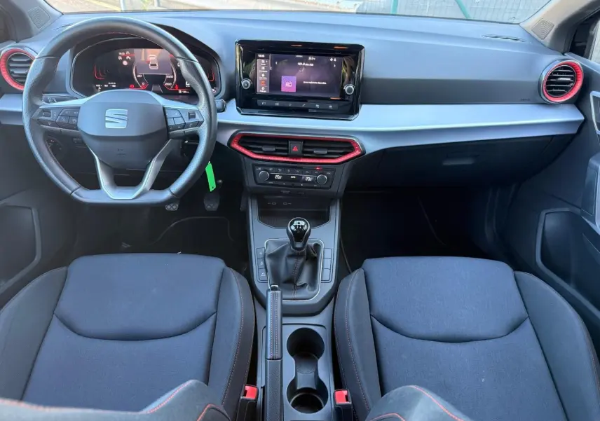 Vue intérieure avant de la SEAT Ibiza 1.0 TSI 95 FR 2025 avec volant cuir, écran tactile central et détails rouges sur les aérateurs.