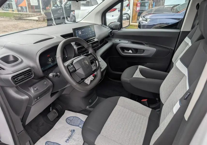 Vue intérieure côté conducteur du Citroën Berlingo blanc 2025, volant cuir multifonctions et sièges tissu bicolores.