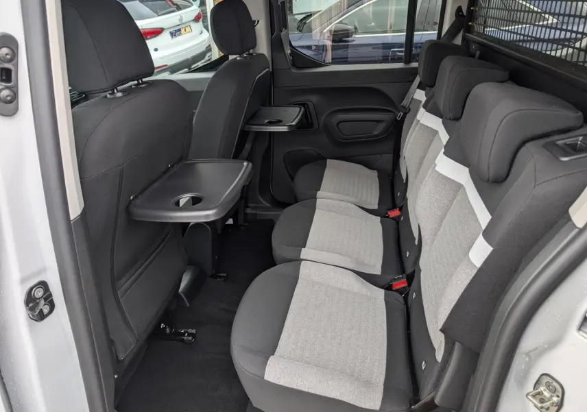 Vue intérieure côté droit sur les trois sièges arrière gris et noir avec tablette rabattable du Citroën Berlingo blanc.