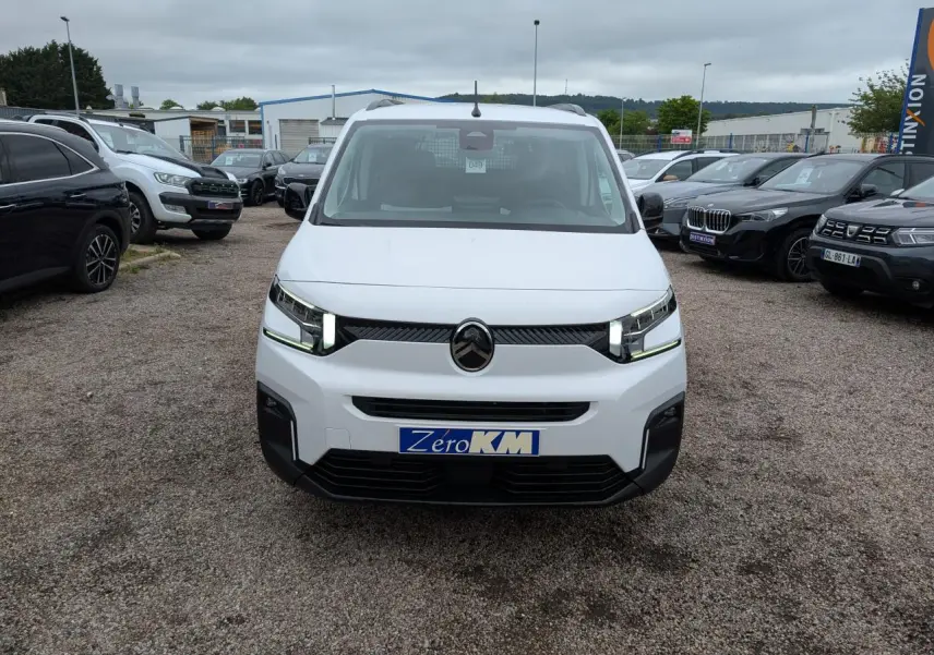 Vue de face du Citroën Berlingo blanc avec calandre noire et phares LED allumés sur un parking.