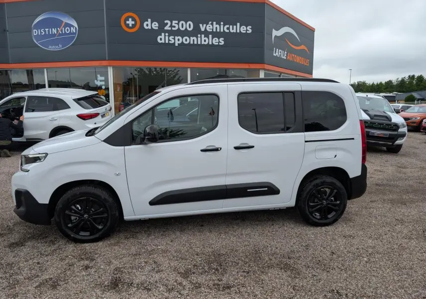 Vue de profil côté gauche d'un Citroën Berlingo blanc avec barres de toit noires et jantes alliage noires.