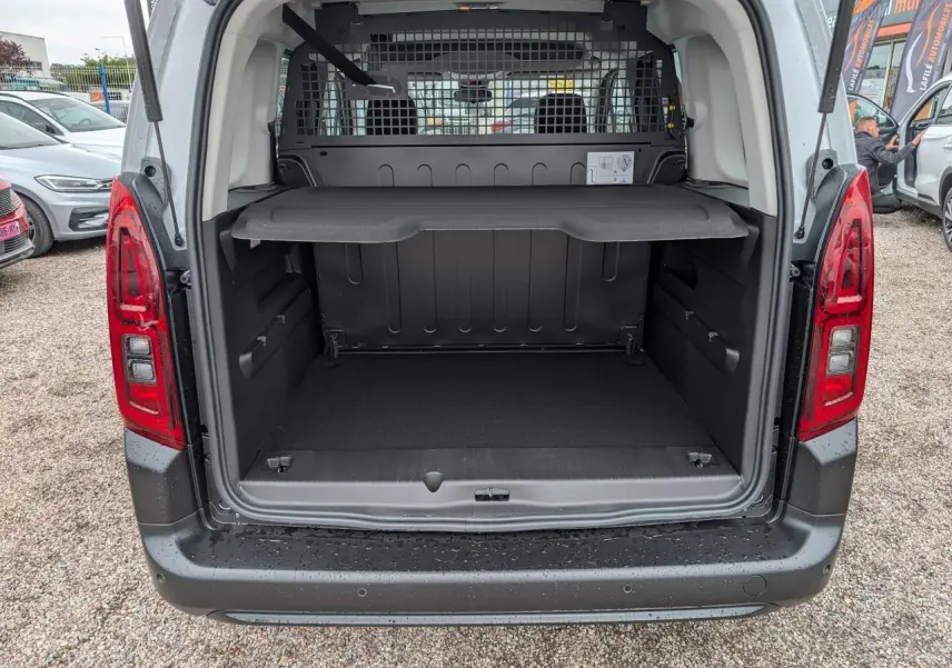 Vue arrière du coffre ouvert du Citroën Berlingo blanc 2025 avec séparation grillagée et tablette de rangement.