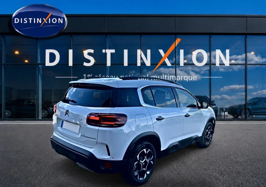 Vue 3/4 arrière droite d'un Citroën C5 Aircross blanc avec jantes alu et vitres arrière teintées devant une vitrine Distinxion.