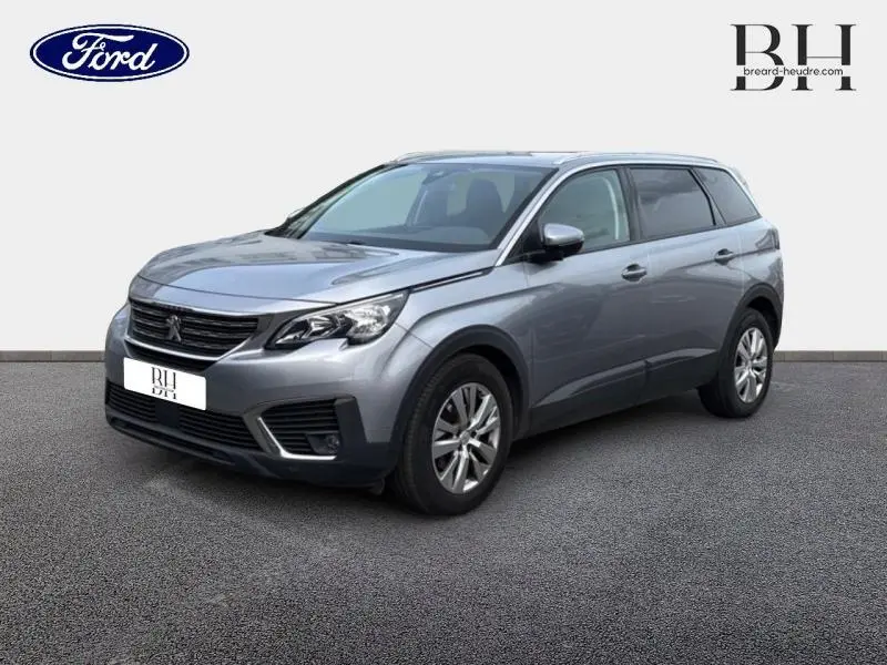 Peugeot 5008 gris Artense en 3/4 avant droit, SUV familial avec jantes alu et barres de toit visibles.