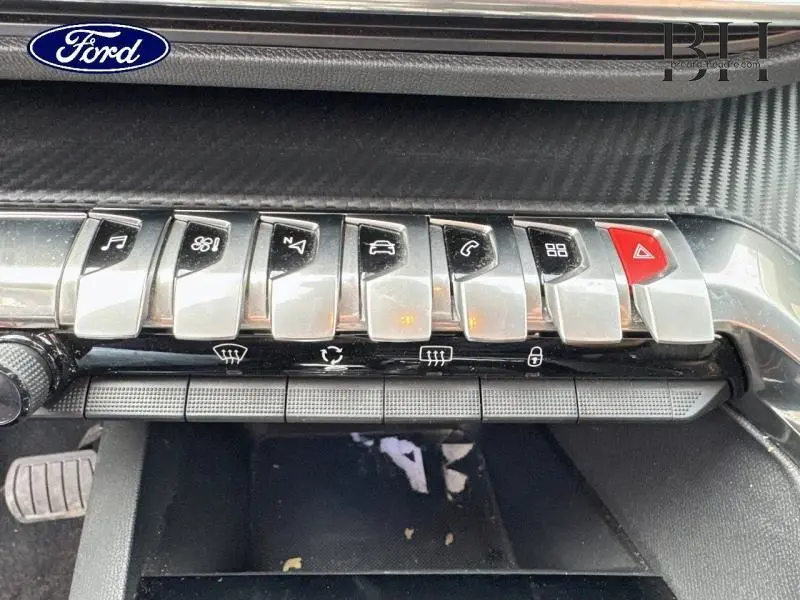 Gros plan sur la rangée de boutons argentés et rouge du tableau de bord avec insert carbone du Peugeot 5008 gris Artense.