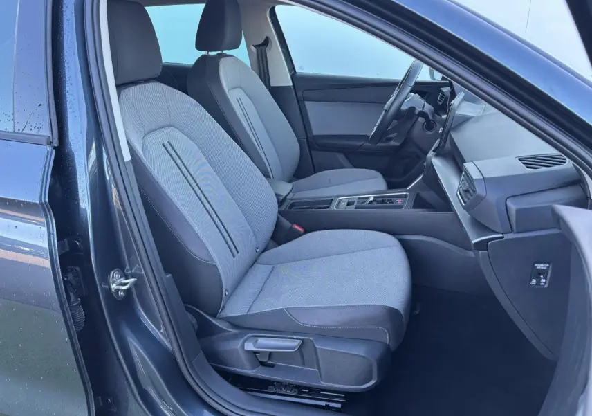 Vue intérieure côté gauche de la SEAT LEON IV gris magnetic, montrant les sièges avant et la console centrale moderne.