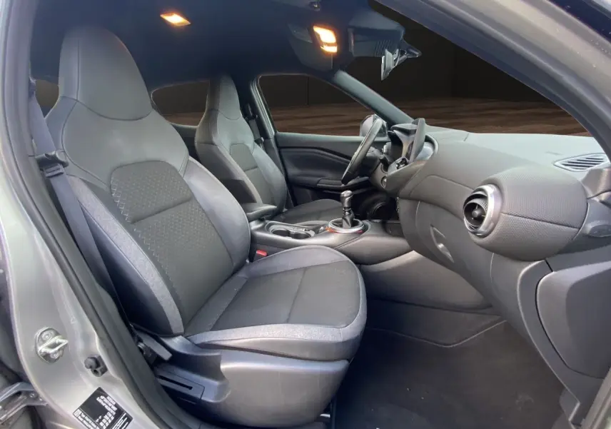 Vue intérieure côté gauche du Nissan Juke 2025, sièges tissu noir avec cuir synthétique et tableau de bord moderne.