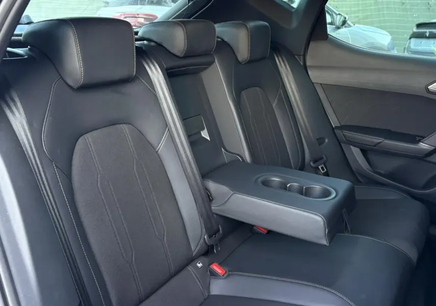 Vue intérieure des sièges arrière noirs bimatière avec accoudoir central rabattable et porte-gobelets de la CUPRA Leon 2025.