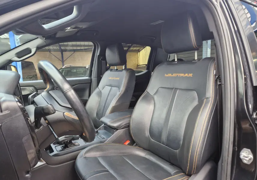 Vue intérieure côté conducteur du Ford Ranger Wildtrak noir 2023, mettant en valeur les sièges cuir avec surpiqûres orange et logo Wildtrak.