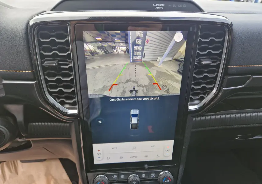 Vue rapprochée de l’écran central tactile du Ford Ranger Wildtrak 2023 noir, affichant la caméra de recul et les commandes climatisation.
