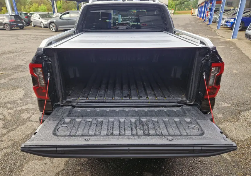 Vue arrière du Ford Ranger Wildtrak noir 2023 avec benne ouverte et rideau de plateau coulissant partiellement visible.