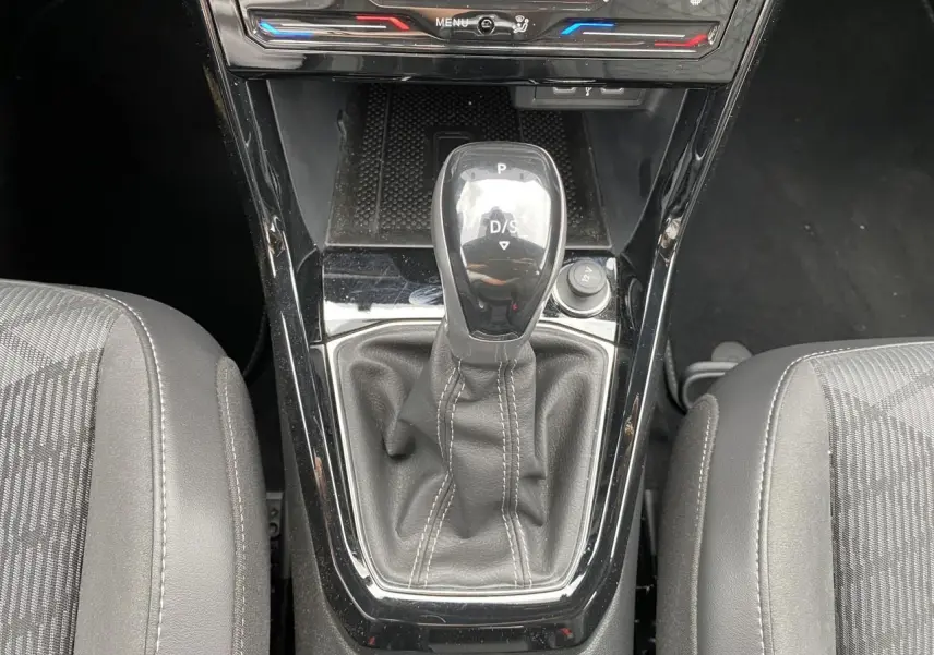 Vue rapprochée de la console centrale du Volkswagen T-Cross gris, mettant en valeur le levier de vitesse DSG7 et les sièges tissu noirs.