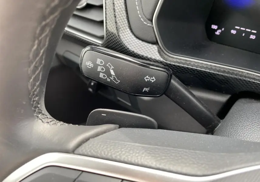 Gros plan sur la manette de clignotant noire du Volkswagen T-Cross 2024, avec volant cuir et tableau de bord gris.