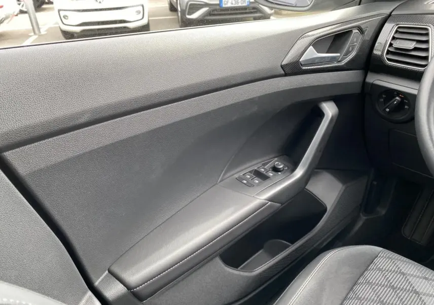 Vue intérieure côté gauche de la porte avant grise du Volkswagen T-Cross 2024 avec commandes de vitres et rétroviseurs.