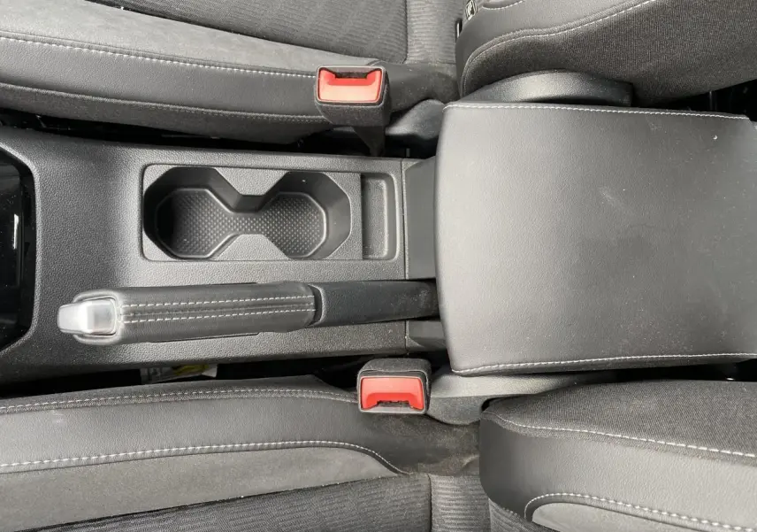 Vue plongeante sur la console centrale noire du Volkswagen T-Cross 2024 avec frein à main manuel et porte-gobelets.