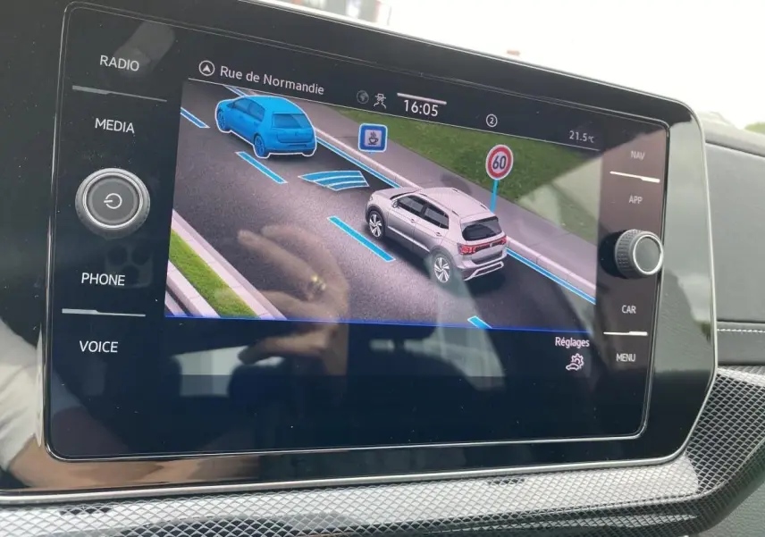 Écran tactile intérieur montrant l’assistance de conduite du Volkswagen T-Cross gris en vue 3/4 arrière sur route.