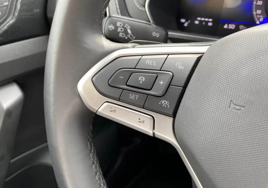 Gros plan sur le volant cuir gris du Volkswagen T-Cross 2024, avec commandes multifonctions et affichage digital en arrière-plan.