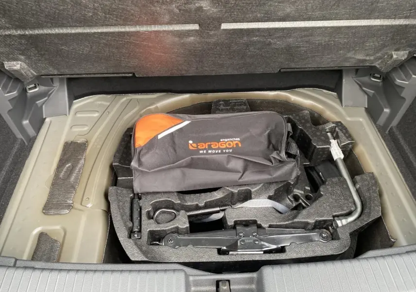 Vue plongeante sur la roue de secours et l’outillage de bord dans le coffre du Volkswagen T-Cross gris 2024.