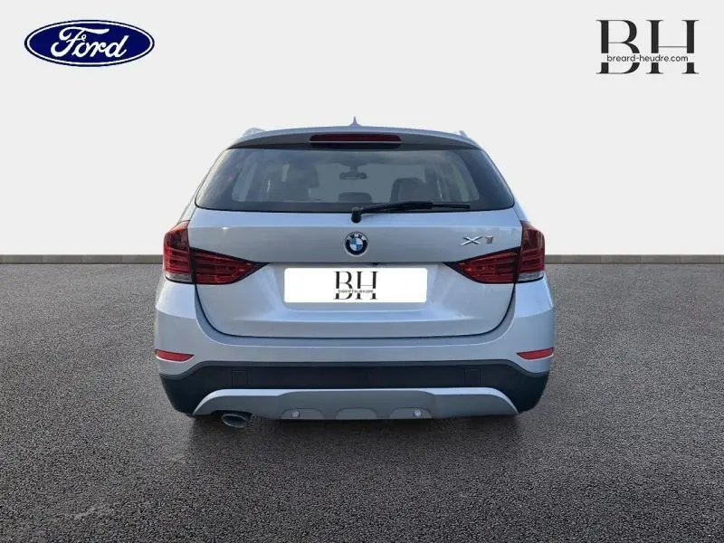 Vue arrière d'une BMW X1 xDrive25dA 2014 en Mineralgrau avec feux arrière rouges et sortie d'échappement chromée visible.