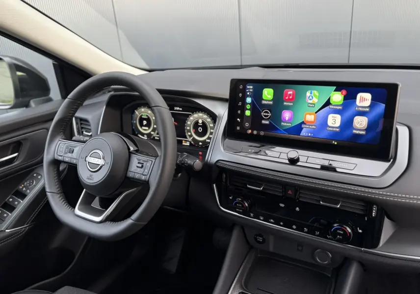 Vue intérieure côté conducteur du Nissan Qashqai gris Ceramic 2025, avec écran tactile large et volant cuir noir.