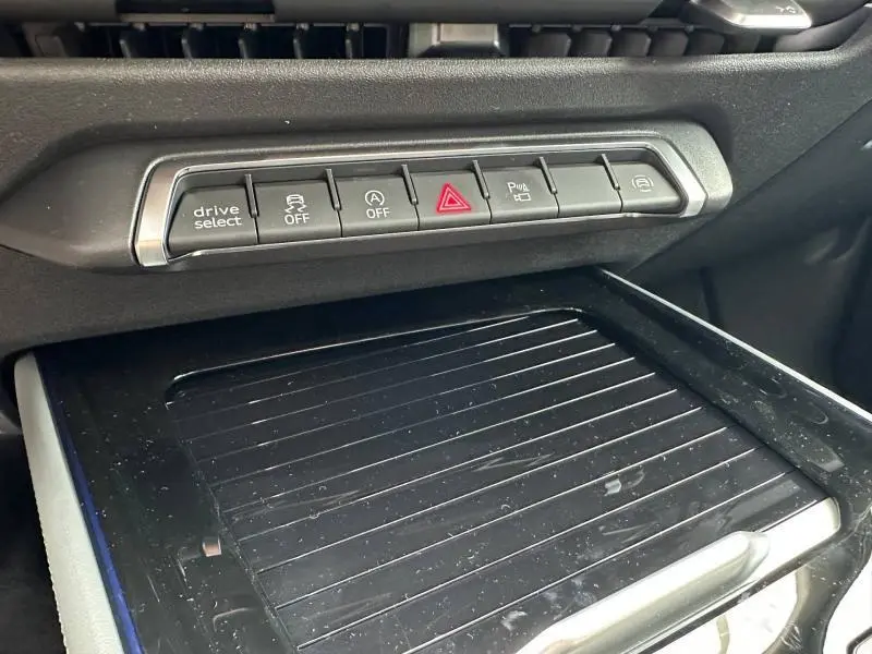 Vue rapprochée de la console centrale noire du Audi Q3 2026 avec boutons de contrôle et surface de rangement striée.