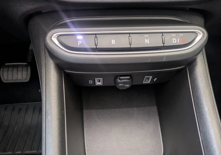 Vue rapprochée de la console centrale noire du Fiat 600 1.2 Hybrid 2025 avec boutons de boîte auto et prises USB visibles.