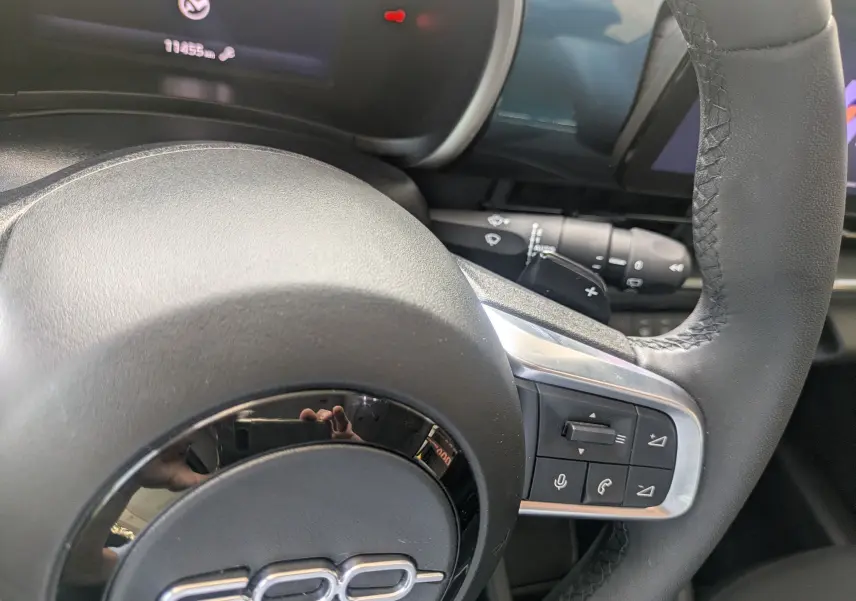 Gros plan sur le volant noir de la Fiat 600 2025 avec commandes intégrées et tableau de bord numérique partiellement visible.