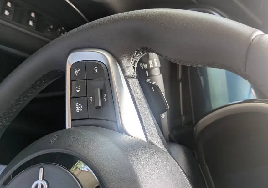 Gros plan sur le volant noir du Fiat 600 1.2 Hybrid 2025, avec commandes intégrées et partie de la portière côté gauche visible.