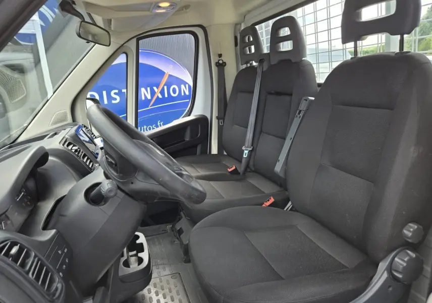 Vue intérieure côté conducteur du Fiat Ducato Fourgon blanc 2022, montrant les sièges noirs et le volant réglable.