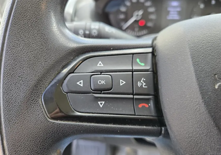 Gros plan sur les commandes gauche du volant noir du Fiat Ducato Fourgon blanc 2022, avec boutons multifonctions.