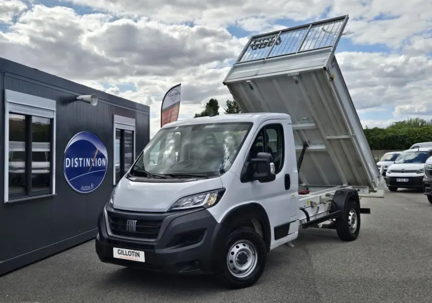 Fiat Ducato Fourgon blanc vu en 3/4 avant droit avec benne arrière relevée sur un parking extérieur.