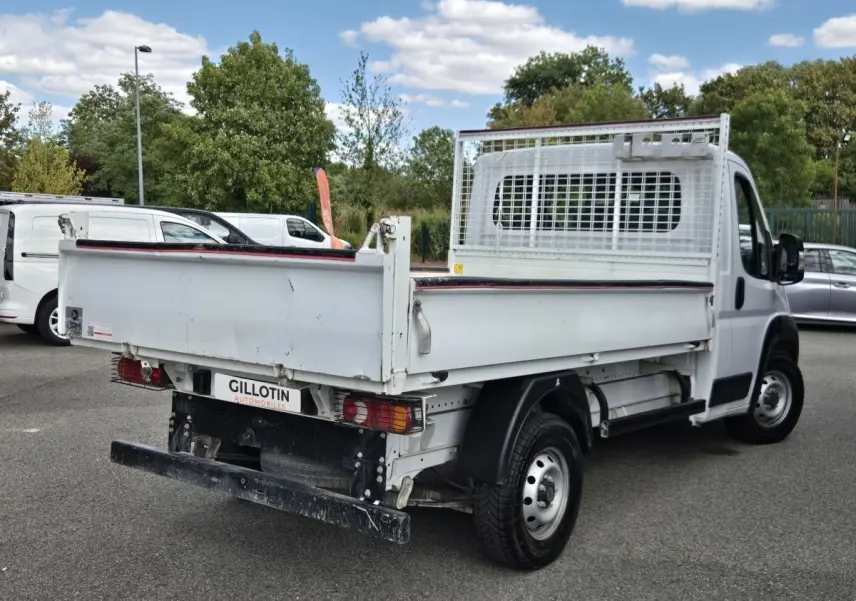 Fiat Ducato Fourgon blanc vu en 3/4 arrière droit, benne basculante avec grille de protection cabine.