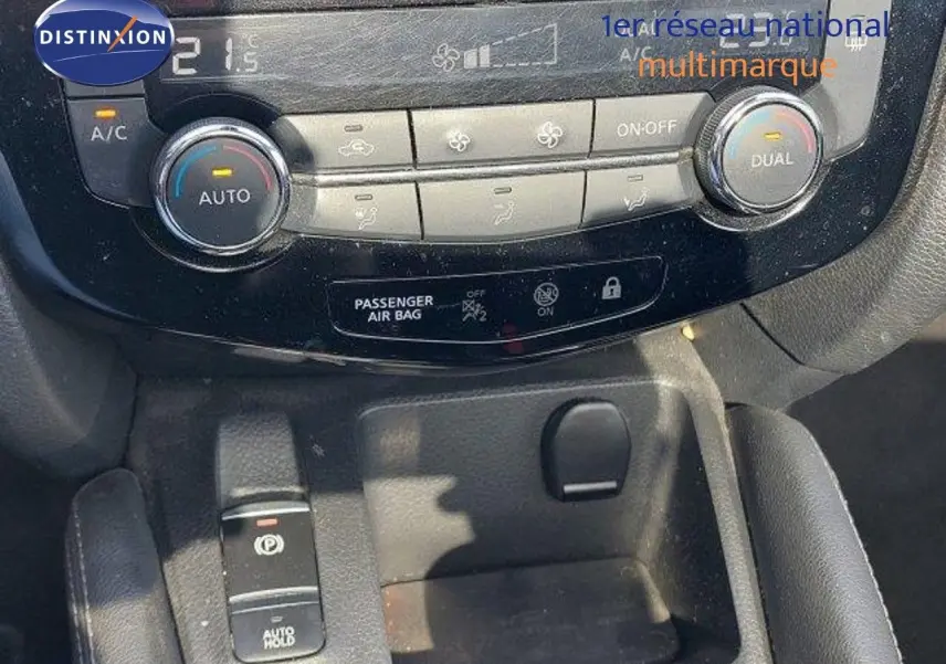 Gros plan sur la console centrale du Nissan Qashqai blanc lunaire, montrant les commandes de climatisation et frein à main électrique.