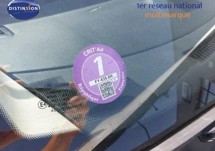 Vue rapprochée du pare-brise d'un Nissan Qashqai blanc lunaire avec vignette Crit'Air 1 apposée côté gauche.