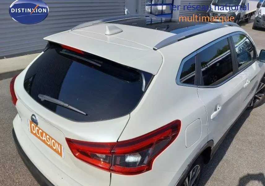 Vue 3/4 arrière droite d'un Nissan Qashqai blanc lunaire métallisé avec vitres teintées et toit équipé d'une antenne requin.