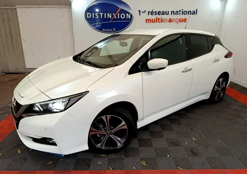 Nissan Leaf blanche vue en 3/4 avant droit dans un showroom avec logo Distinxion en arrière-plan.