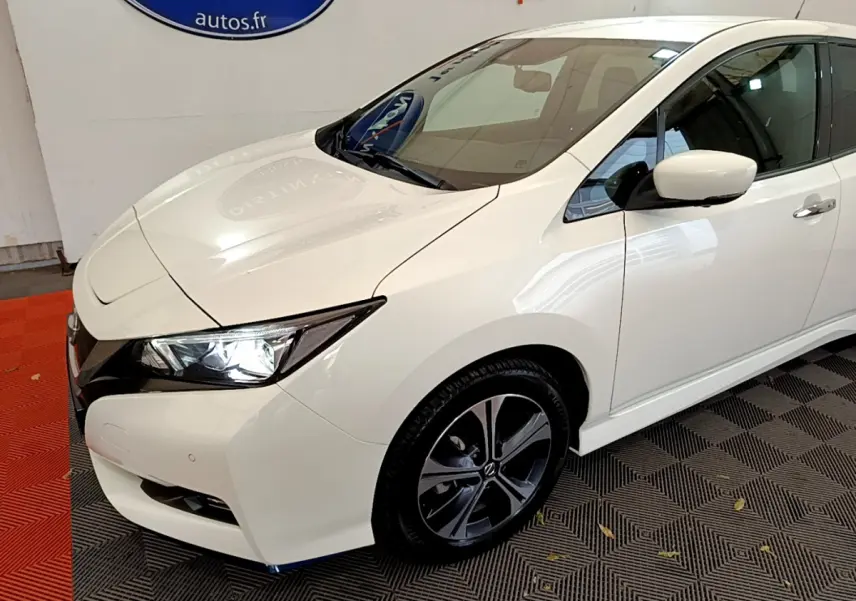 Nissan Leaf blanche vue de 3/4 avant droit, phare LED allumé et jante alliage sombre au design moderne.