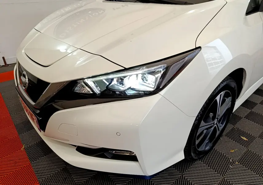 Vue 3/4 avant droit d'une Nissan Leaf blanche avec phares LED allumés et jantes alliage distinctives.