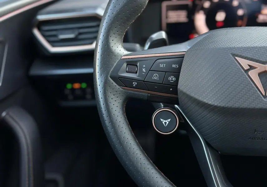 Gros plan sur le volant noir perforé de la CUPRA Leon 2025 avec logo cuivre et commandes intégrées.