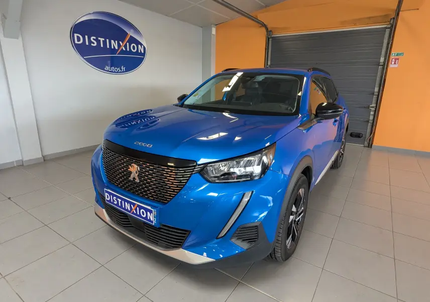 Peugeot 2008 bleu en 3/4 avant droit, avec calandre noire et jantes alliage bicolores, en intérieur showroom.