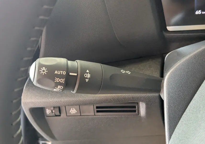 Gros plan sur la manette de commande des phares et clignotants à gauche du volant dans l'habitacle gris du Citroën C4 Hybrid 2025.