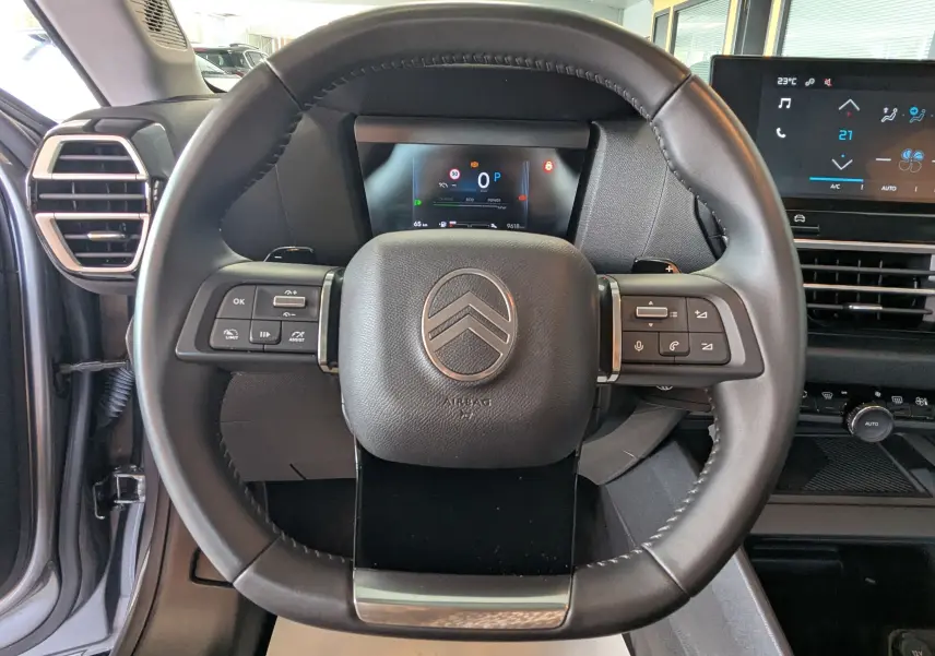 Vue rapprochée du volant noir de la Citroën C4 Hybrid 145 E-DCS6 Plus avec tableau de bord digital et commandes intégrées.