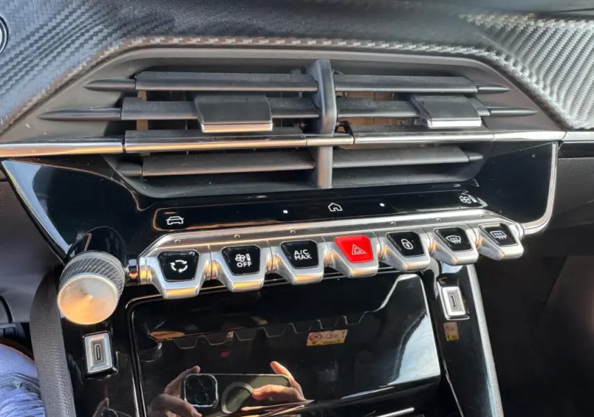 Gros plan sur la console centrale du Peugeot 2008 Hybrid noir, avec commandes climatisation et boutons chromés.