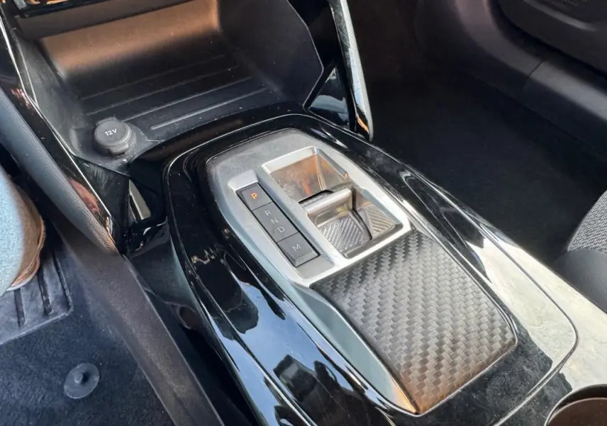 Gros plan sur la console centrale noire brillante du Peugeot 2008 Hybrid 136 e-DCS6 Allure avec levier de boîte auto.