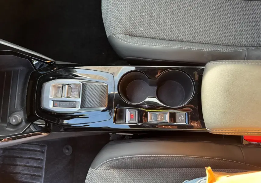 Vue plongeante sur la console centrale noire brillante du Peugeot 2008 Hybrid 136 avec commandes de boîte auto et porte-gobelets.